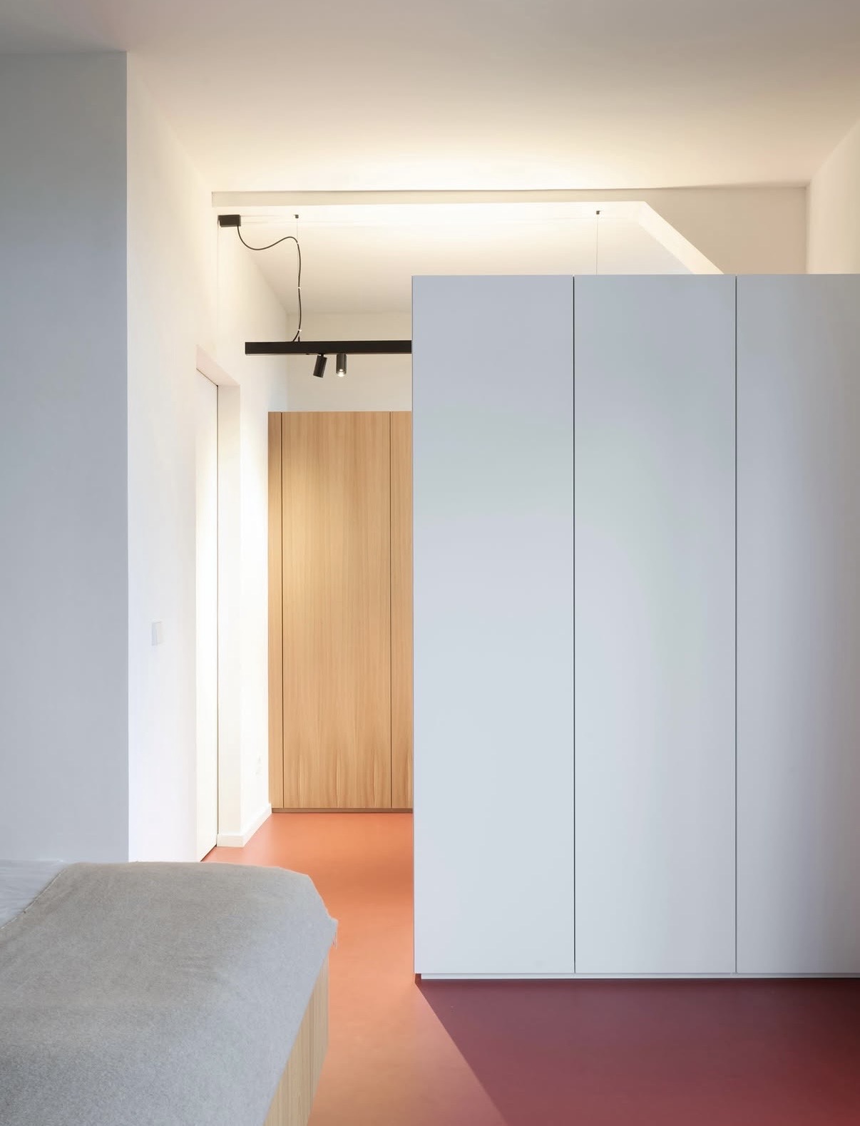 Schlafzimmer mit weißem Einbauschrank, Tür aus Rüster und warmem Terrakotta-Bodenbelag