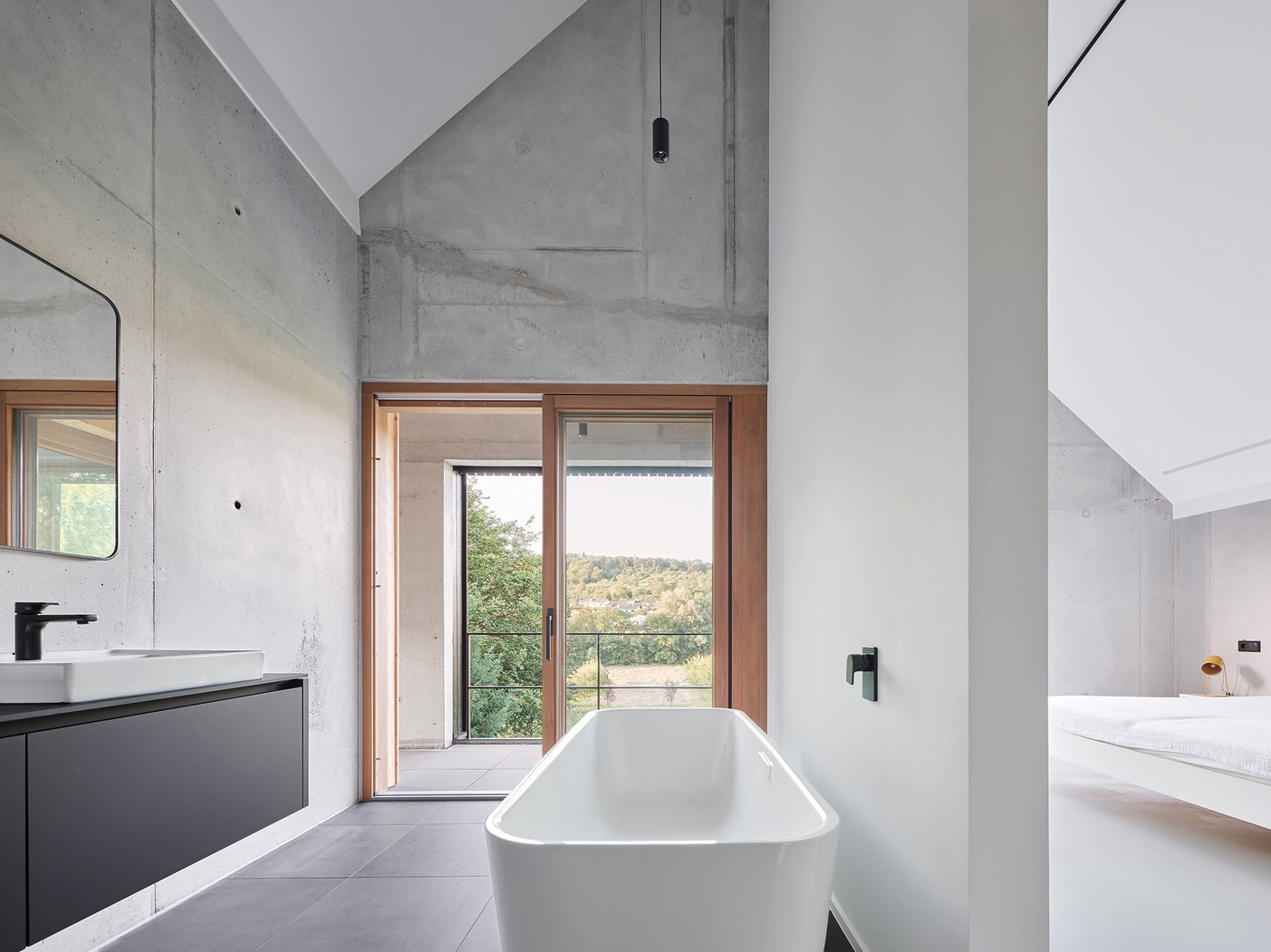 Haus RO – Badezimmer mit freistehender Badewanne, schwarzem Waschtisch und bodentiefer Holzschiebetür zum Balkon