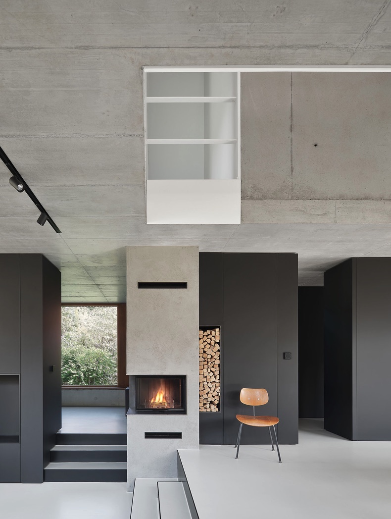 Haus RO – Kaminwand aus Beton mit Holzlager, schwarzen Einbauschränken und klassischem Holzstuhl