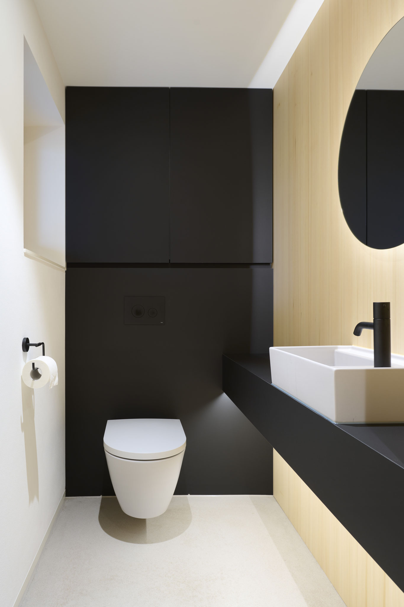 Gäste-WC mit schwarzer Möbelfront, Eichenholz und rundem Spiegel