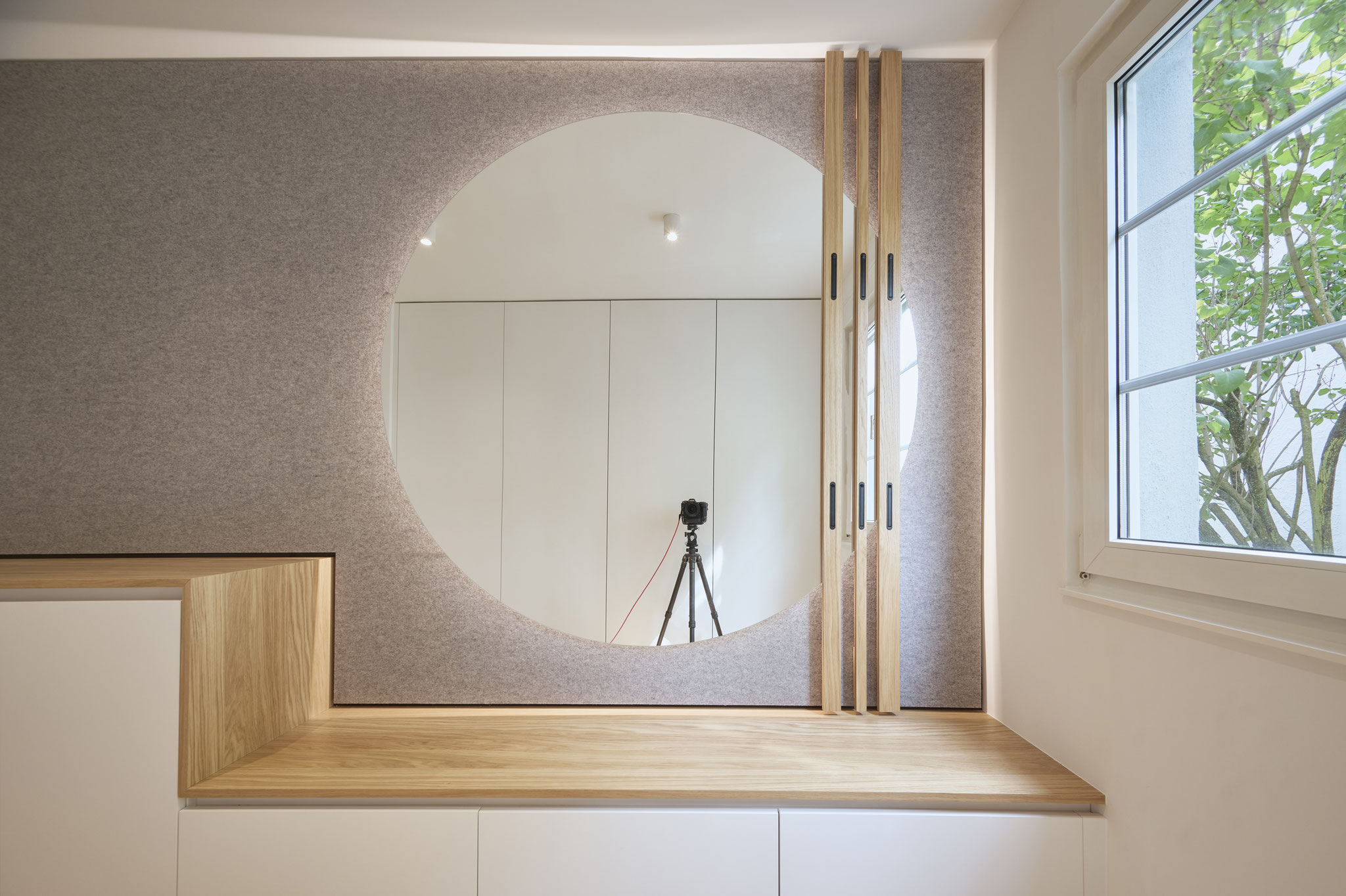 Innenausbau-Detail mit Filzwand, rundem Durchblick und Eichenbank
