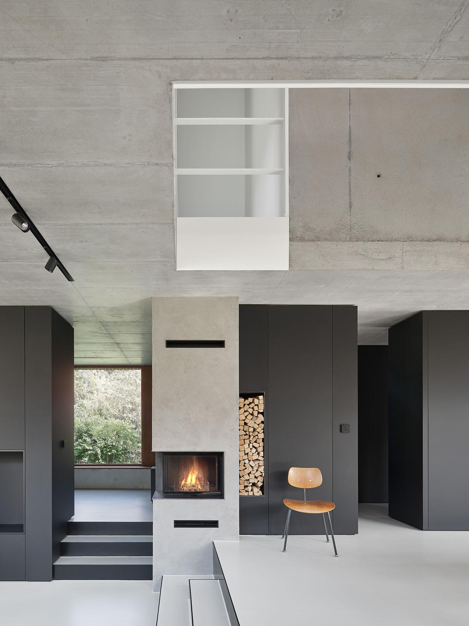 Wohnraum mit Sichtbeton, schwarzen Einbauschränken und Kamin